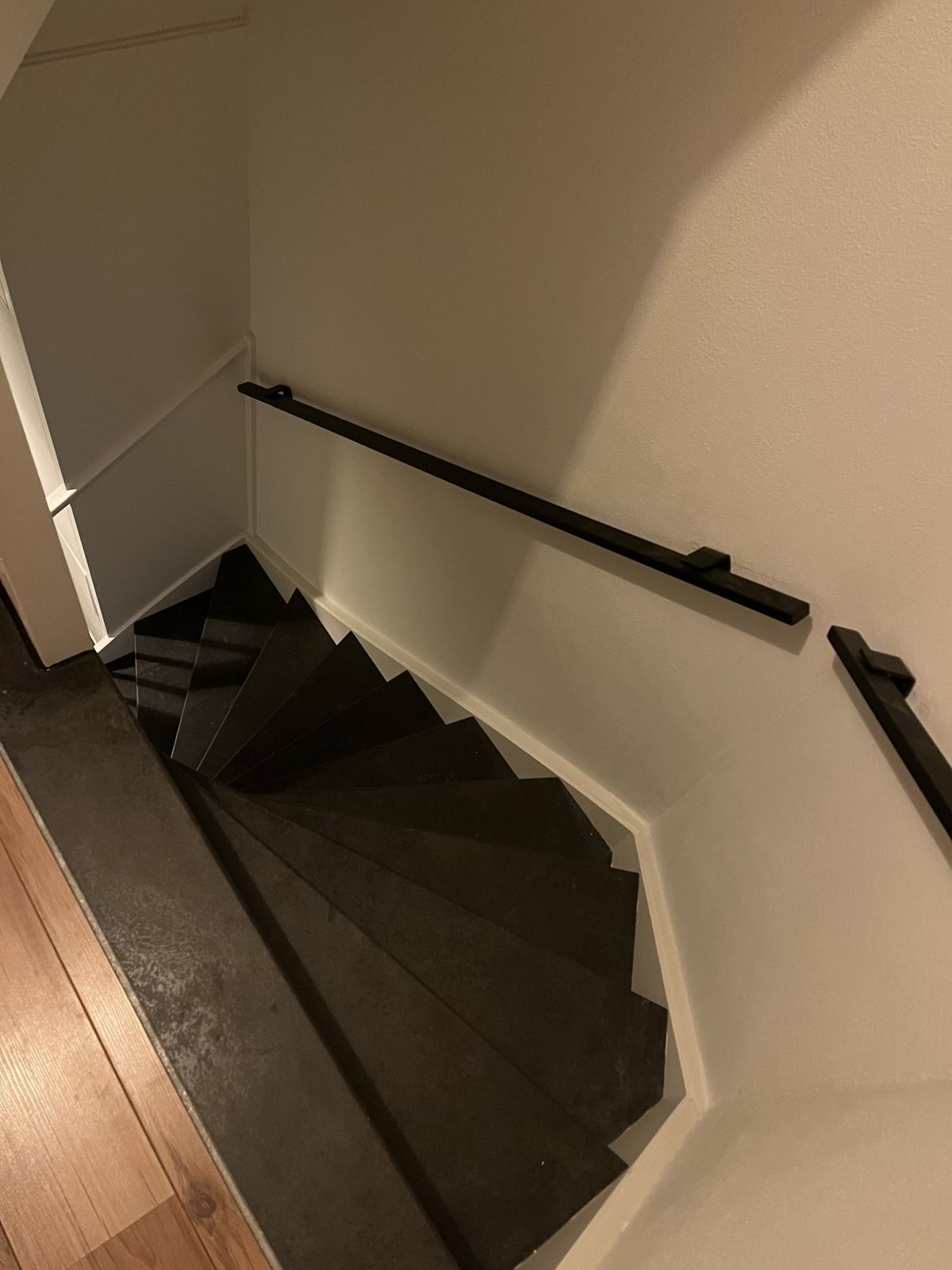 Antraciet trap met zwarte leuning langs een witte wand