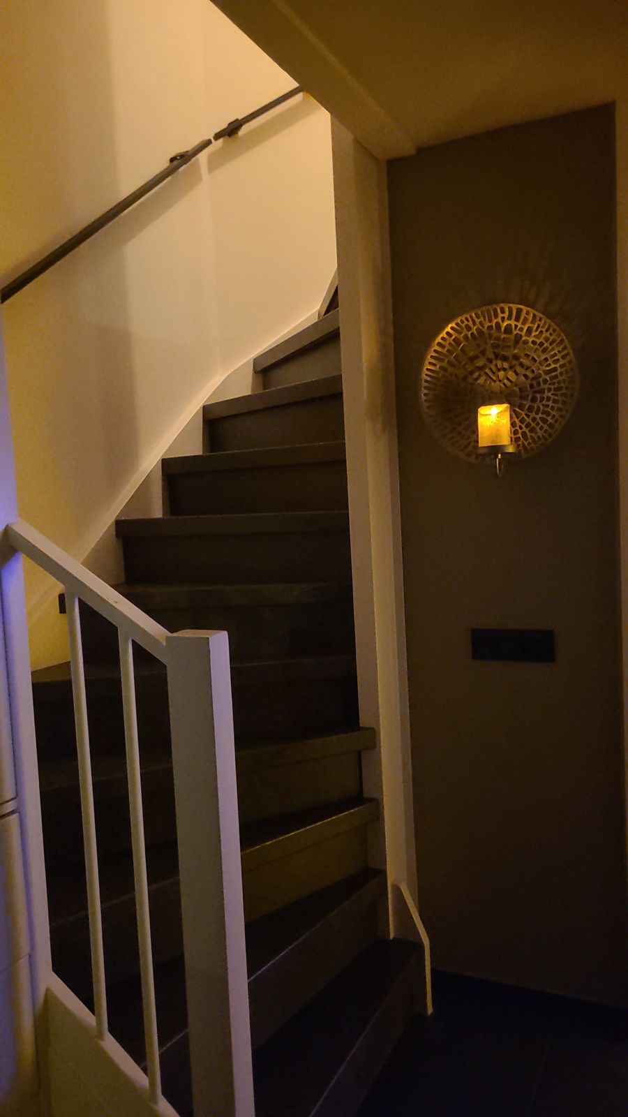 Donkere trap met witte balustrade en een warme wandlamp in de avond